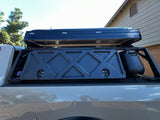 Overlanding truck bed with black rooftop tent, storage box, & water tank on a rack. Great for your next RV rental.