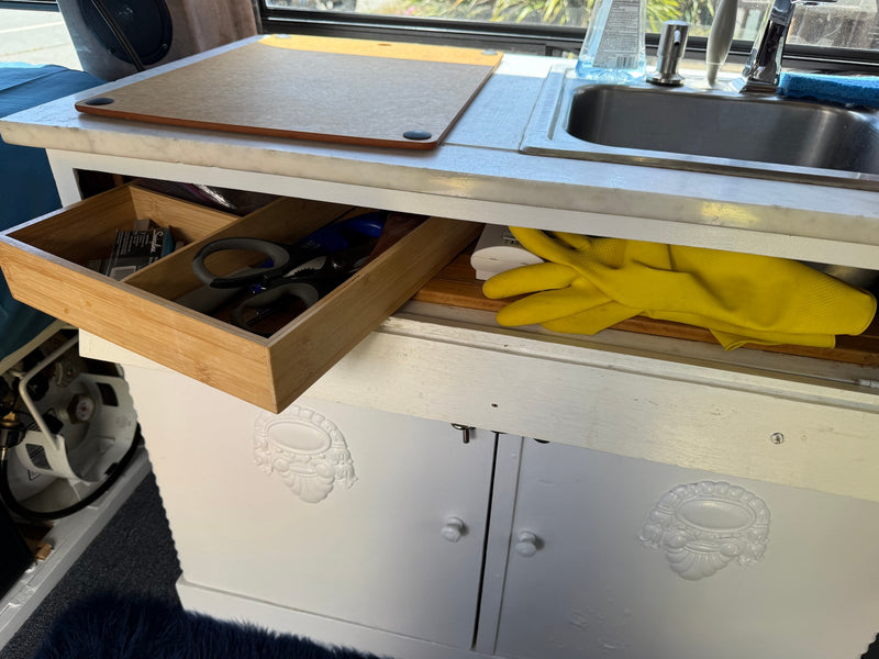This RV rental features a compact kitchen with a sink, cutting board, open drawer with scissors, and yellow gloves. — photo 1