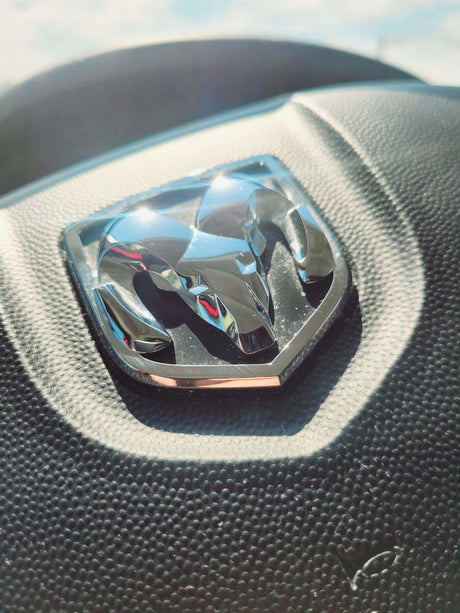 Close-up of a chrome Ram logo on a black textured steering wheel, perfect for your RV rental adventure.