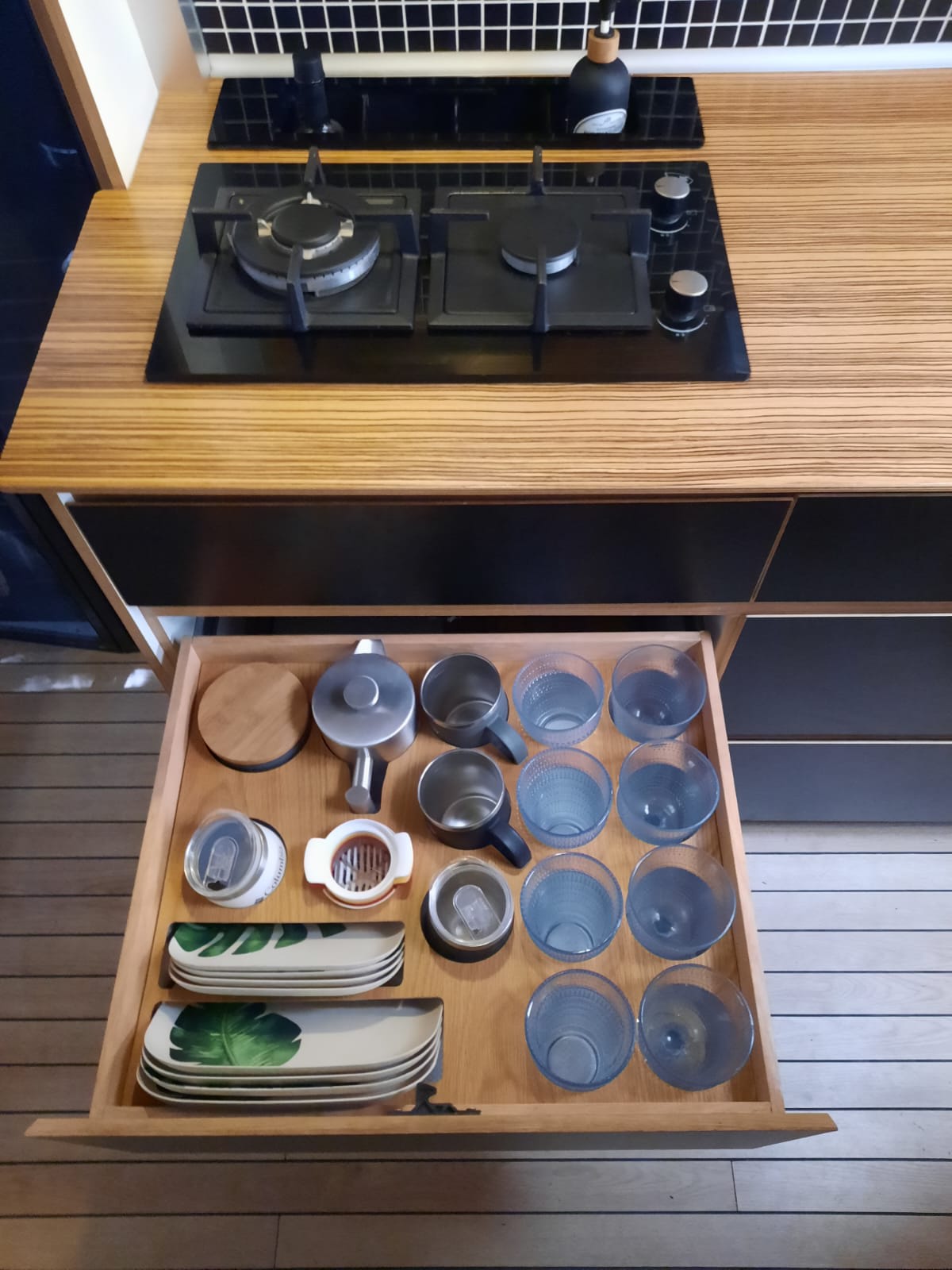 RV rental kitchen: Open drawer reveals plates, glasses, mugs. Countertop features a modern gas cooktop. — photo 11