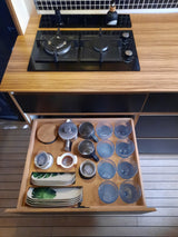 RV rental kitchen: Open drawer reveals plates, glasses, mugs. Countertop features a modern gas cooktop.