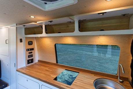 Interior of an RV rental: features a sleek kitchen with wooden counters, induction cooktop, sink, and ample storage.