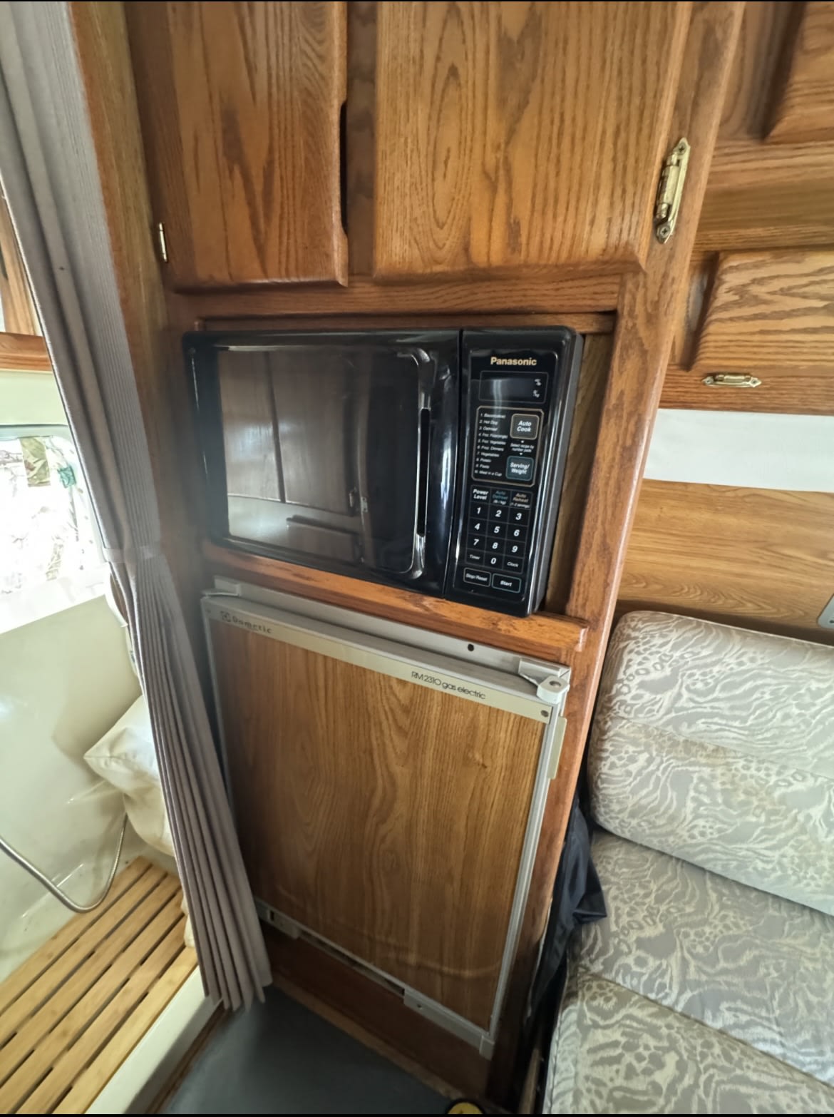 RV rental kitchen: Panasonic microwave & Dometic gas-electric fridge built into warm wooden cabinets. Cozy and functional. — photo 16