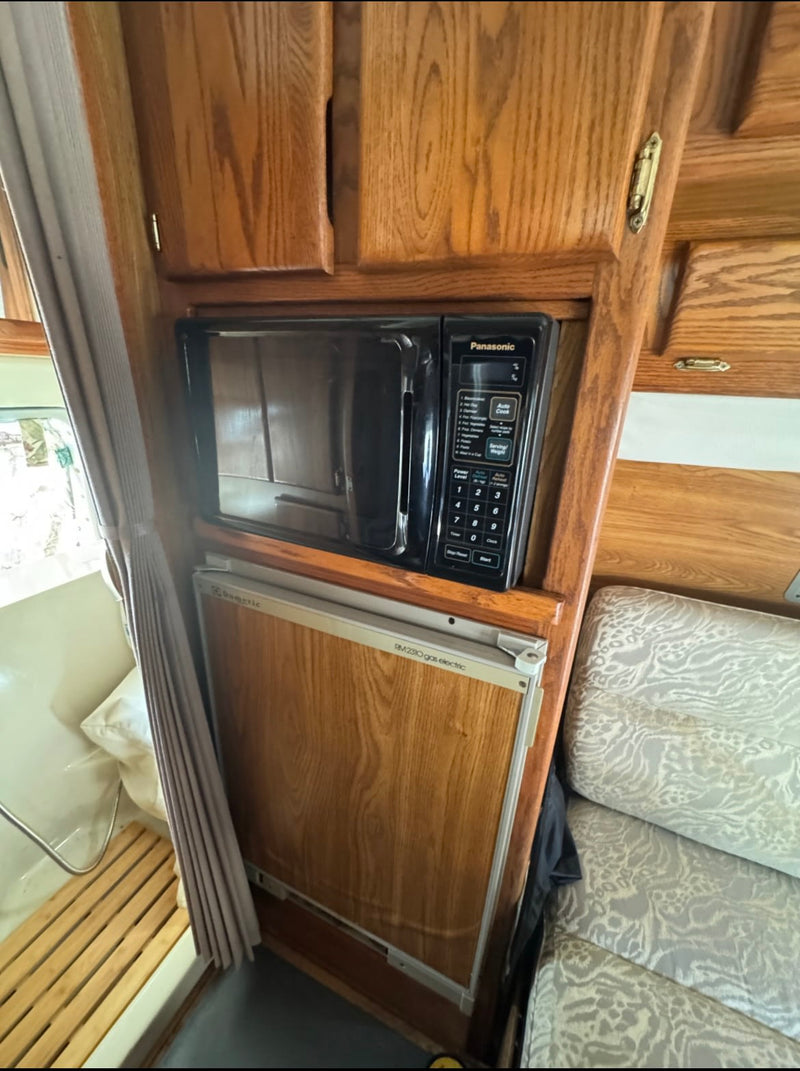 RV rental kitchen: Panasonic microwave & Dometic gas-electric fridge built into warm wooden cabinets. Cozy and functional. — photo 16
