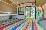 This RV rental offers a compact, cozy bedroom with overhead storage & a view of pine trees. Perfect for adventure!