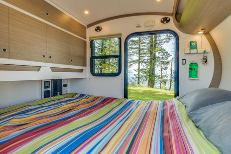 This RV rental offers a compact, cozy bedroom with overhead storage & a view of pine trees. Perfect for adventure!