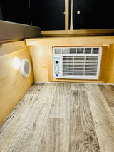 This RV rental interior offers a Keystone AC unit, LED light, and vent. Light wood walls and flooring create a cozy, functional space.