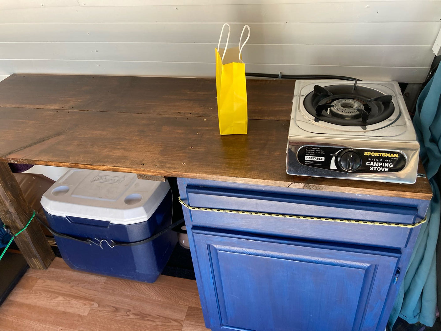 RV rental interior showing a compact kitchen with a portable camping stove, cooler, and blue storage cabinet.