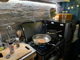 This compact RV rental kitchen features a gas stove cooking a meal, with a sink and spices ready for adventure.