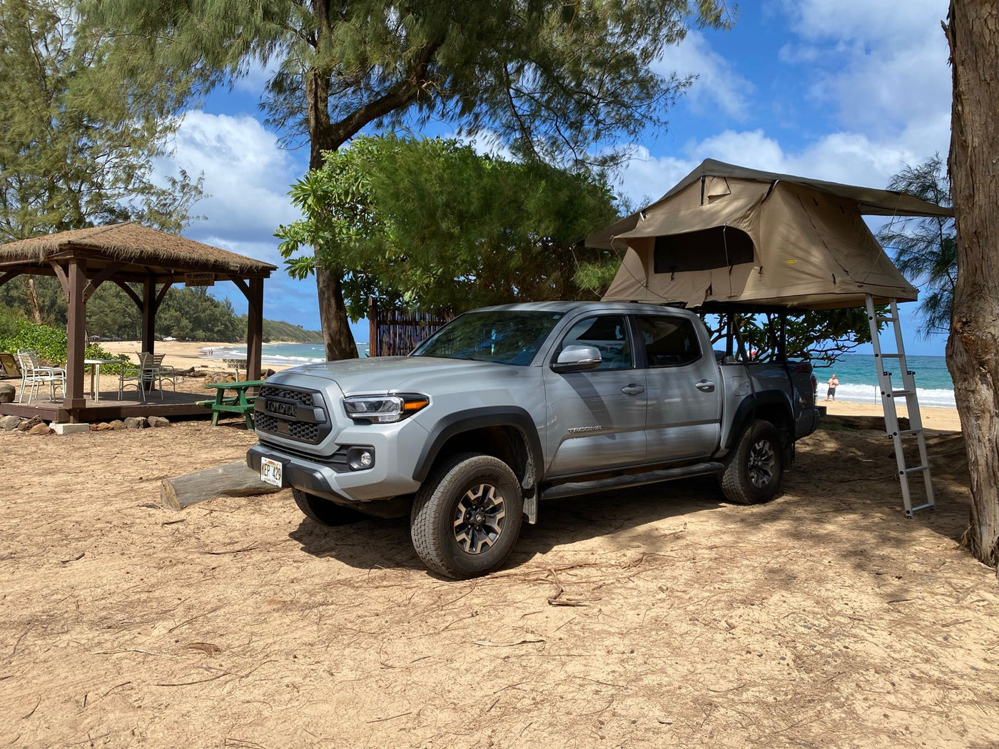 RV rental: A gray Toyota Tacoma pickup truck with a rooftop tent is parked on a sandy Hawaiian beach by the ocean. — photo 2