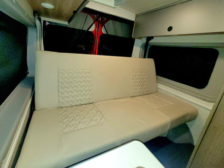 Comfortable RV rental interior with spacious bench seating, overhead storage, and a small table, perfect for travel.