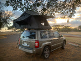 RV rental: Tan Jeep Patriot with rooftop tent, set up for camping at sunset. Perfect for adventure travel!