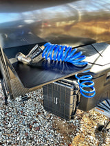 RV rental ready: A blue coiled hose and nozzle on a black outdoor shelf with a storage case.