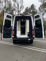 White RV rental van with rear doors open, showing its cozy, converted interior. Ready for your next outdoor adventure.