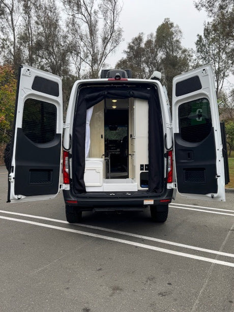 White RV rental van with rear doors open, showing its cozy, converted interior. Ready for your next outdoor adventure.
