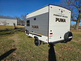 A white Forest River Puma Camping Edition travel trailer, perfect for an rv rental, sits on grass under a clear blue sky.