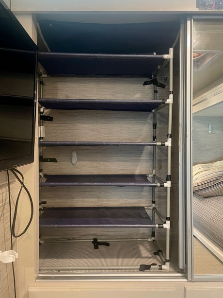 RV rental bedroom with custom-built, multi-tier PVC pipe and fabric shelving for organized storage, beside a TV.