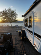 RV rental by a lake at sunset. A white camper, tree, and picnic table make for a peaceful waterfront camping spot.