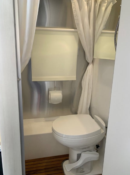 This RV rental's compact wet bath includes a toilet, shower curtain, and window blind, providing essential amenities. — photo 4