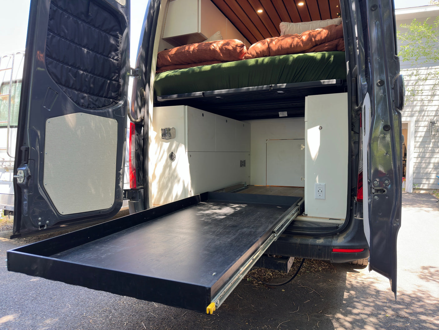 RV rental camper van interior featuring a pull-out gear tray, bed, and custom storage layout.
