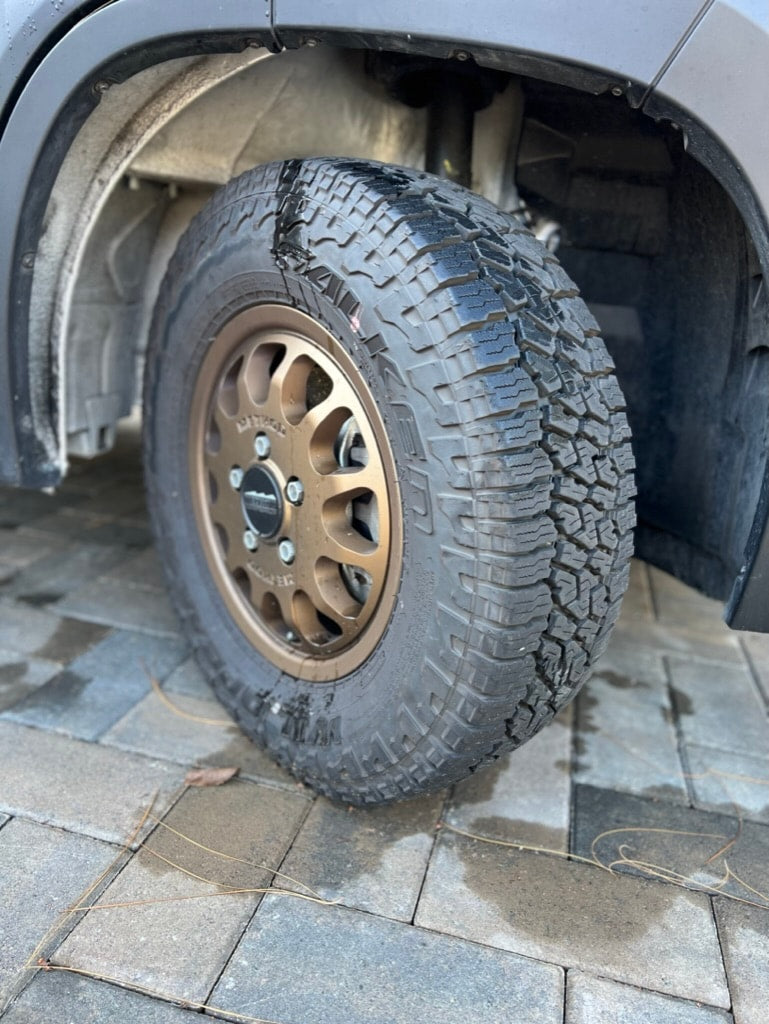 A robust, wet all-terrain tire on a bronze Method wheel, part of an RV rental, ready for any adventure. Paved ground visible. — photo 6