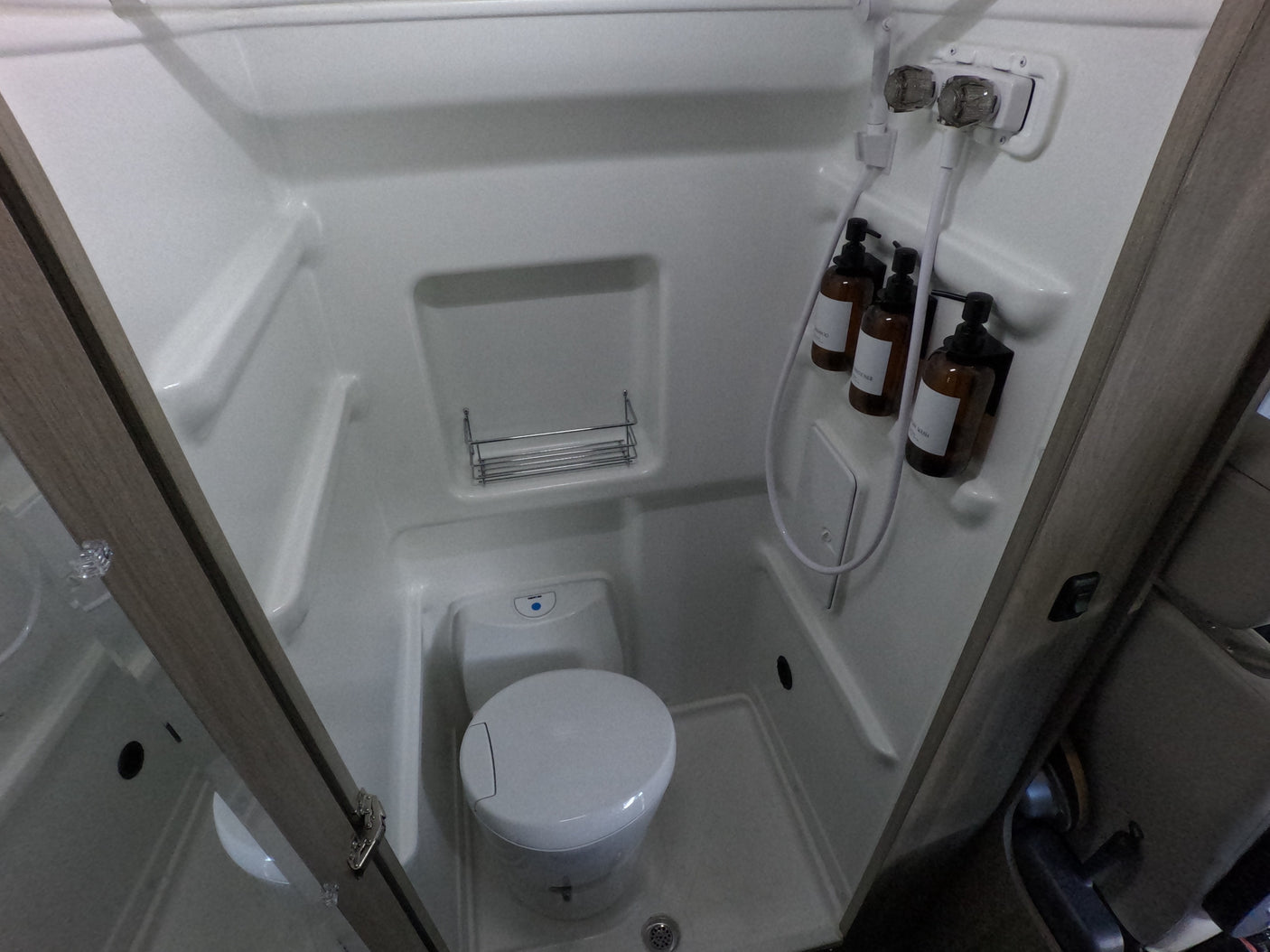 Compact RV rental wet bath with an integrated shower and toilet, featuring hanging toiletries and a small storage shelf.