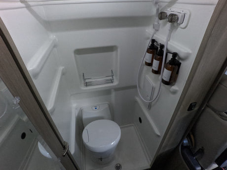 Compact RV rental wet bath with an integrated shower and toilet, featuring hanging toiletries and a small storage shelf.