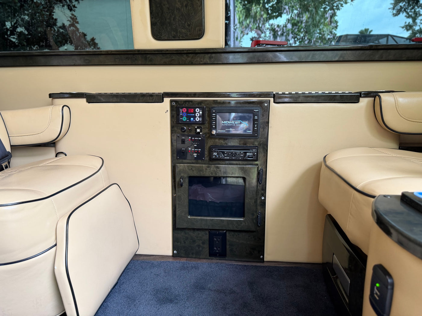 Inside this luxury **rv rental**: tan leather seats, dark wood console with screen, Blu-ray, climate controls, & power outlets. — photo 15