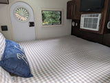 Cozy rv rental interior: checkered bed, blue pillow, outdoor window view, circular door window, AC, and TV.