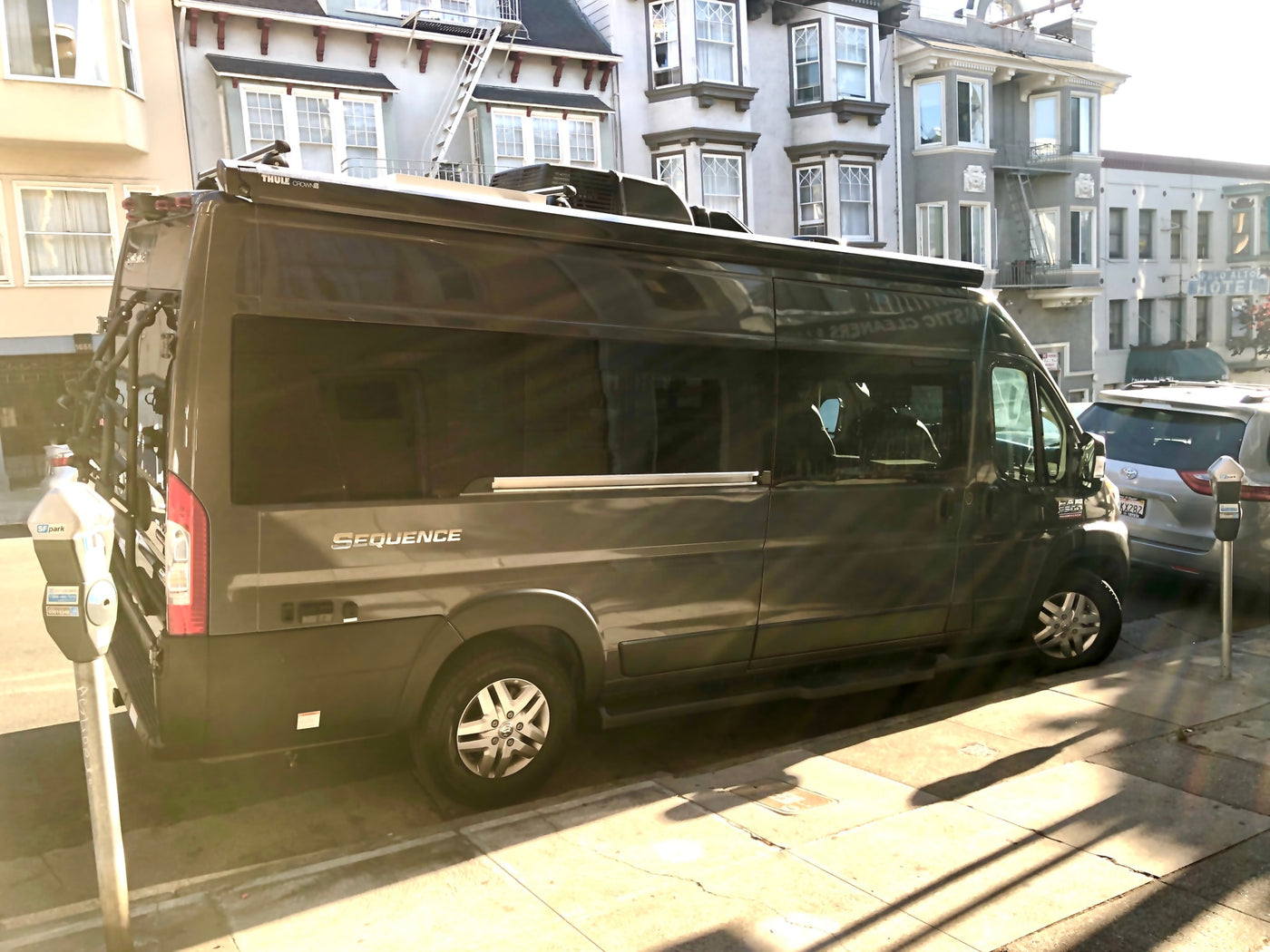A dark gray Thor Sequence camper van, appearing to be an **RV rental**, is parked curbside on a sunny city street. — photo 15