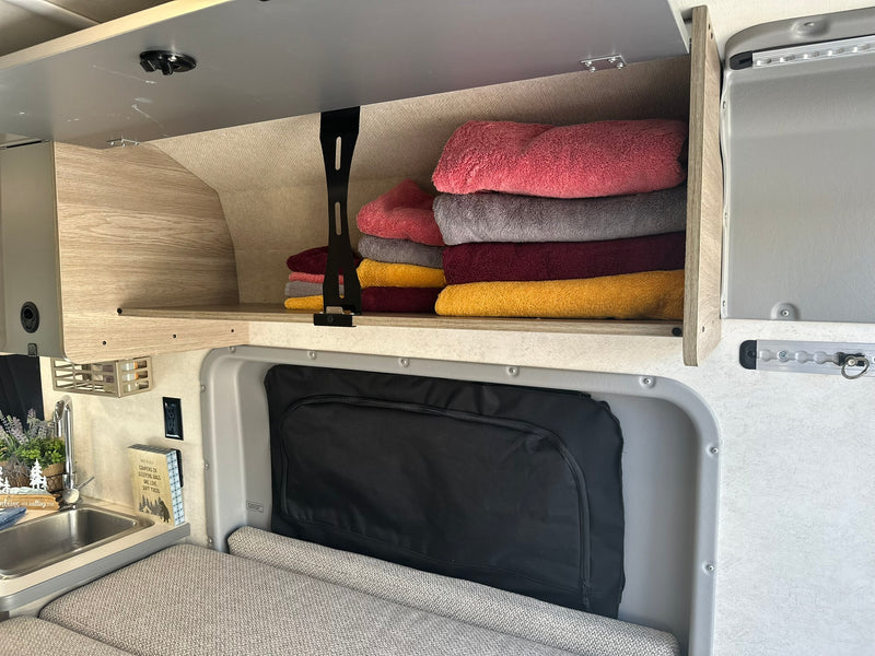 Inside an RV rental: folded towels in an overhead cabinet, compact kitchen sink, and cozy seating/bed area. — photo 4