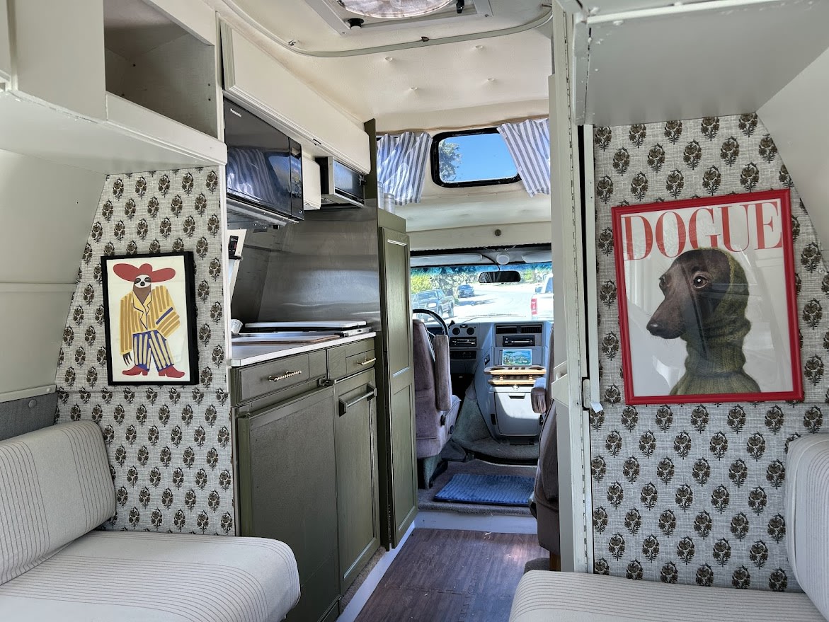 Cozy and personalized RV rental interior with custom sloth and 'DOGUE' art, featuring a compact kitchen.