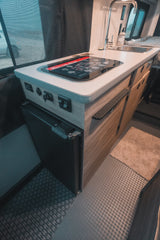 Modern rv rental kitchen area: counter, sink, cooktop, fridge. Features power outlets, cabinet storage, and screen window.