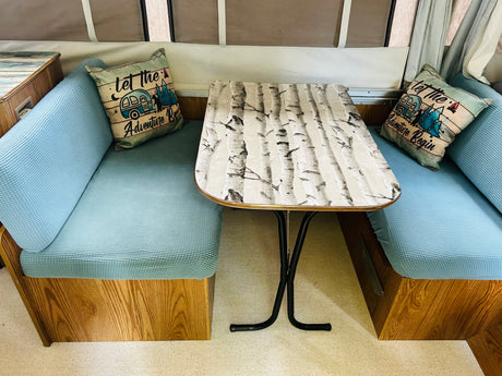 Cozy RV rental dinette featuring a birch tree table, textured blue cushions, and adventure pillows, ideal for travel.