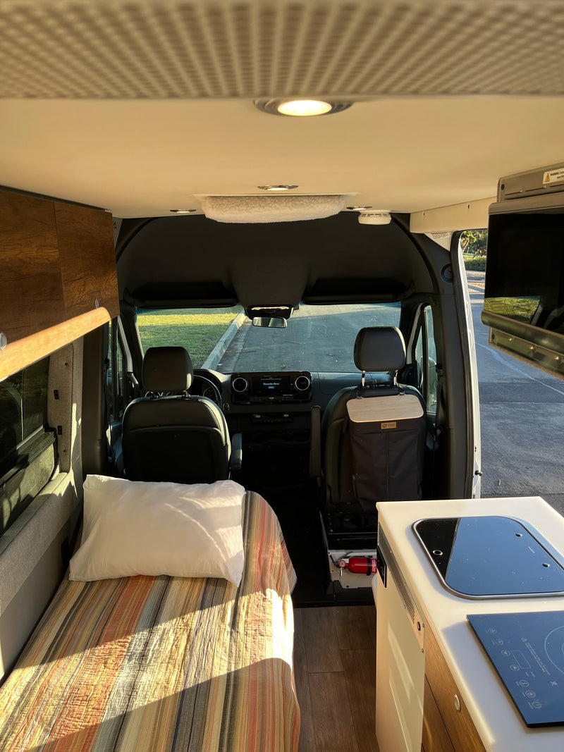 Bright rv rental interior showing a cozy bed, compact kitchen area, and the driver's cabin upfront. — photo 11