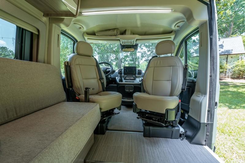 Inside a modern RV rental: Beige front seats, dashboard, and side bench in a bright camper van interior. — photo 10
