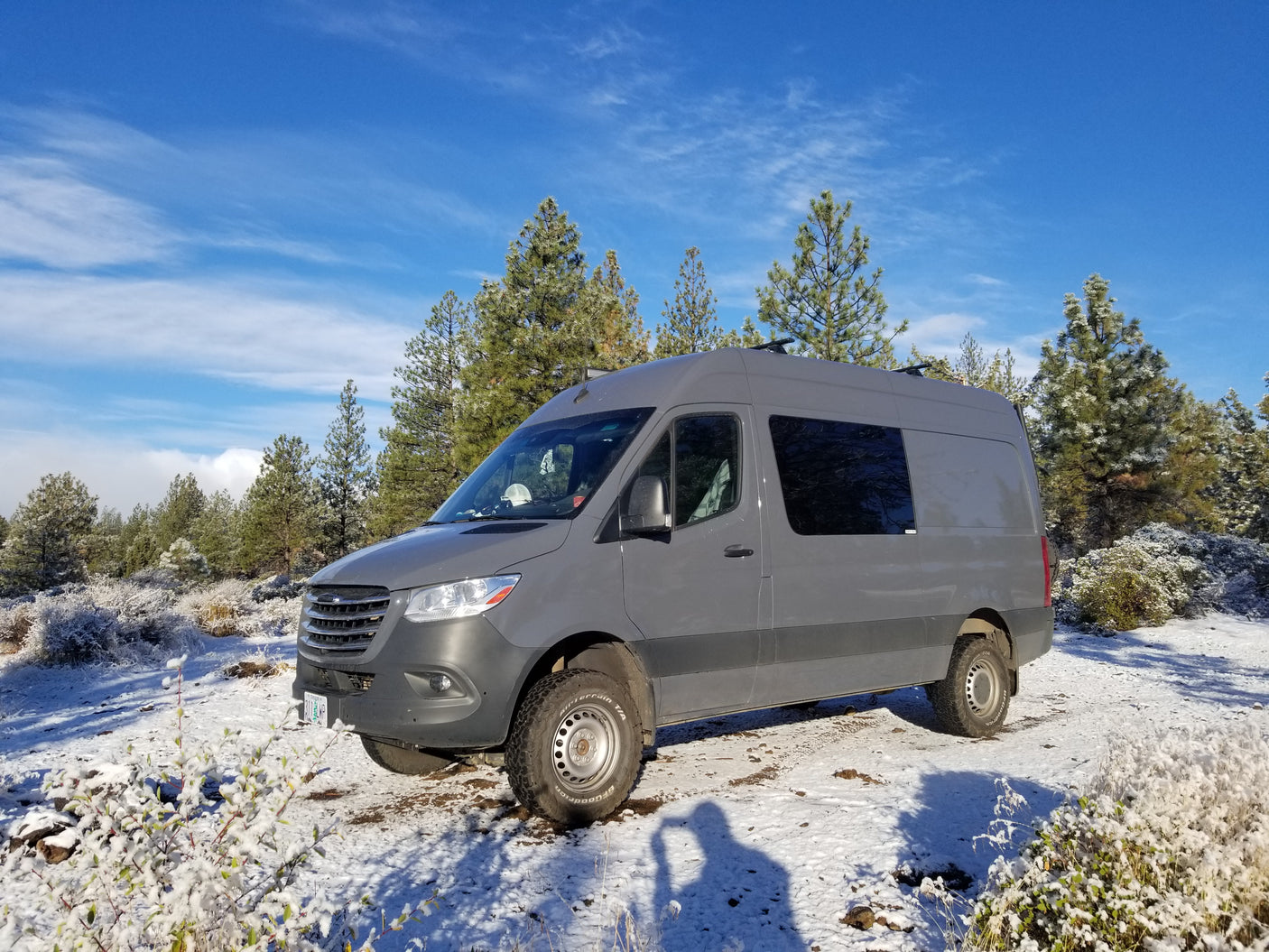 Grey Sprinter camper van **rv rental** in a snowy forest. Enjoy winter adventures with this off-road-ready vehicle.