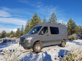 Grey Sprinter camper van **rv rental** in a snowy forest. Enjoy winter adventures with this off-road-ready vehicle.