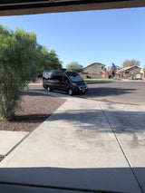 Black camper van **rv rental** parked on a residential street, with a colorful playground in the background under a clear blue sky.