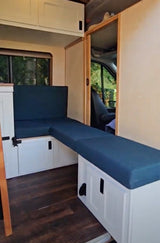 Modern RV rental conversion with versatile L-shaped seating/bed, ample storage, and warm wood flooring.