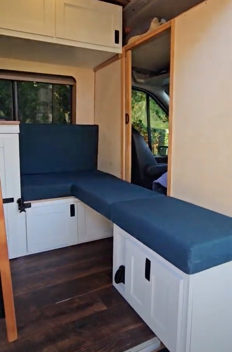 Modern RV rental conversion with versatile L-shaped seating/bed, ample storage, and warm wood flooring.