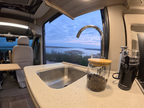 Experience the best of an RV rental: a compact kitchen, fresh coffee, and a picturesque lake view from your cozy camper.