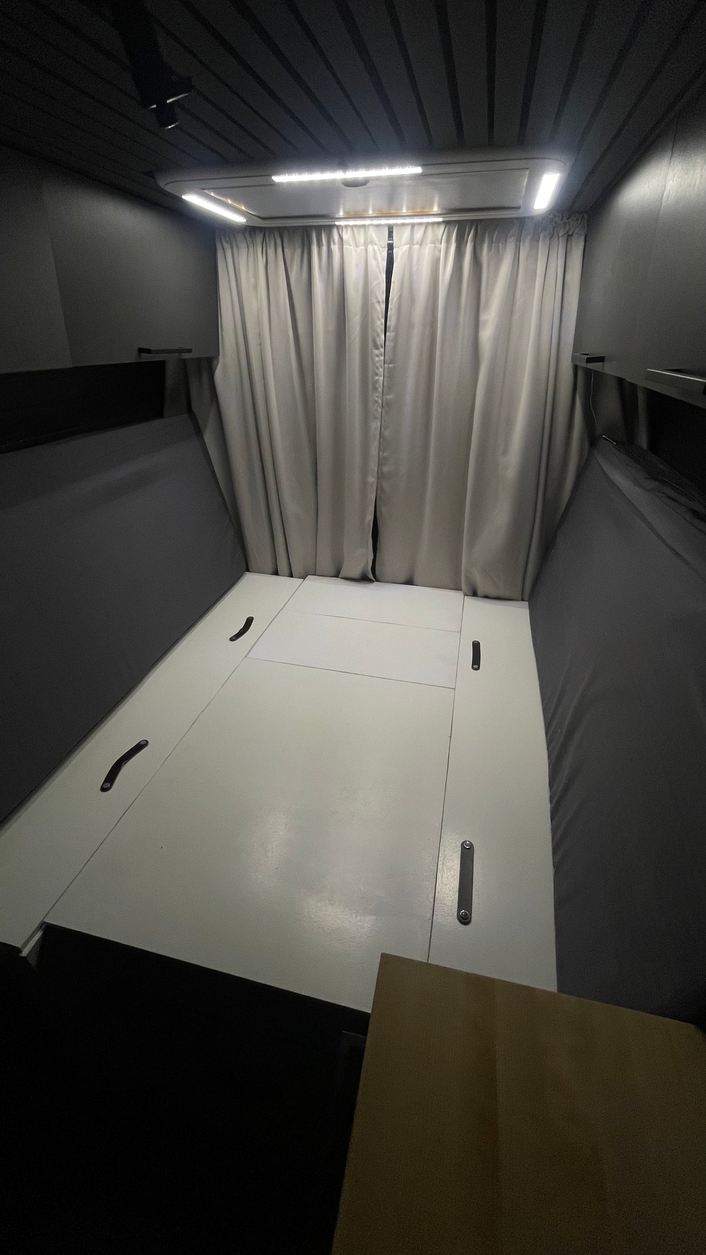 Spacious RV rental interior with convertible floor for sleeping/storage, gray cushions, and light-blocking curtains. Bright LED lighting.