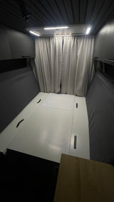 Spacious RV rental interior with convertible floor for sleeping/storage, gray cushions, and light-blocking curtains. Bright LED lighting.
