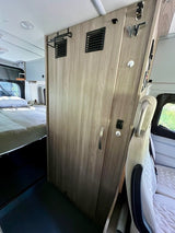 Explore this RV rental's camper van interior: compact bed, central storage with vents, and front seating.