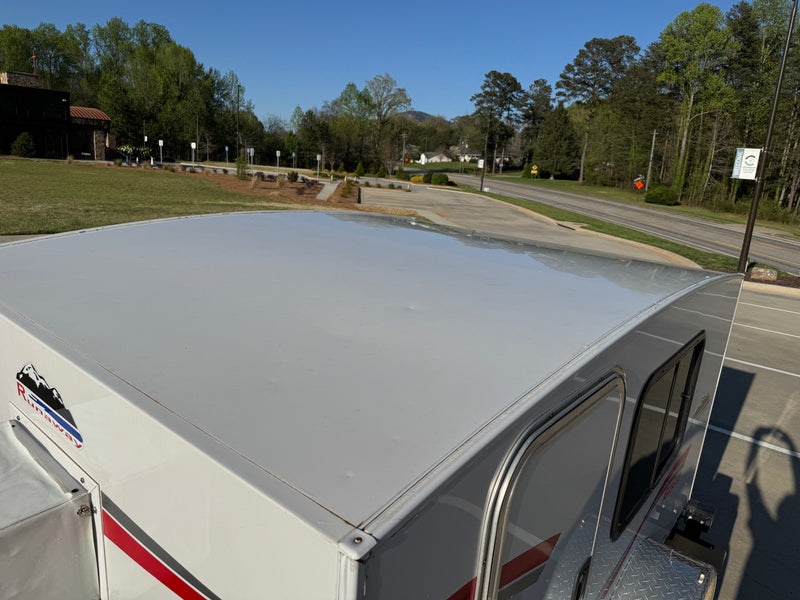 Runaway camper RV rental close-up: white roof and side panels with a scenic background of trees, a road, and distant buildings. — photo 5