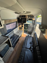 Spacious luxury rv rental interior featuring black leather seating, wood flooring, a TV, and the driver's area.