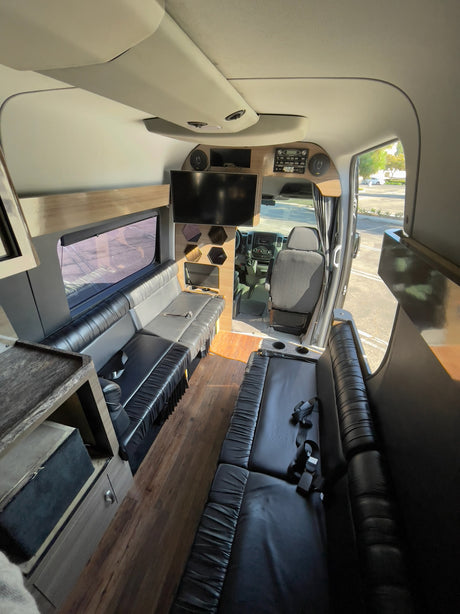 Spacious luxury rv rental interior featuring black leather seating, wood flooring, a TV, and the driver's area.