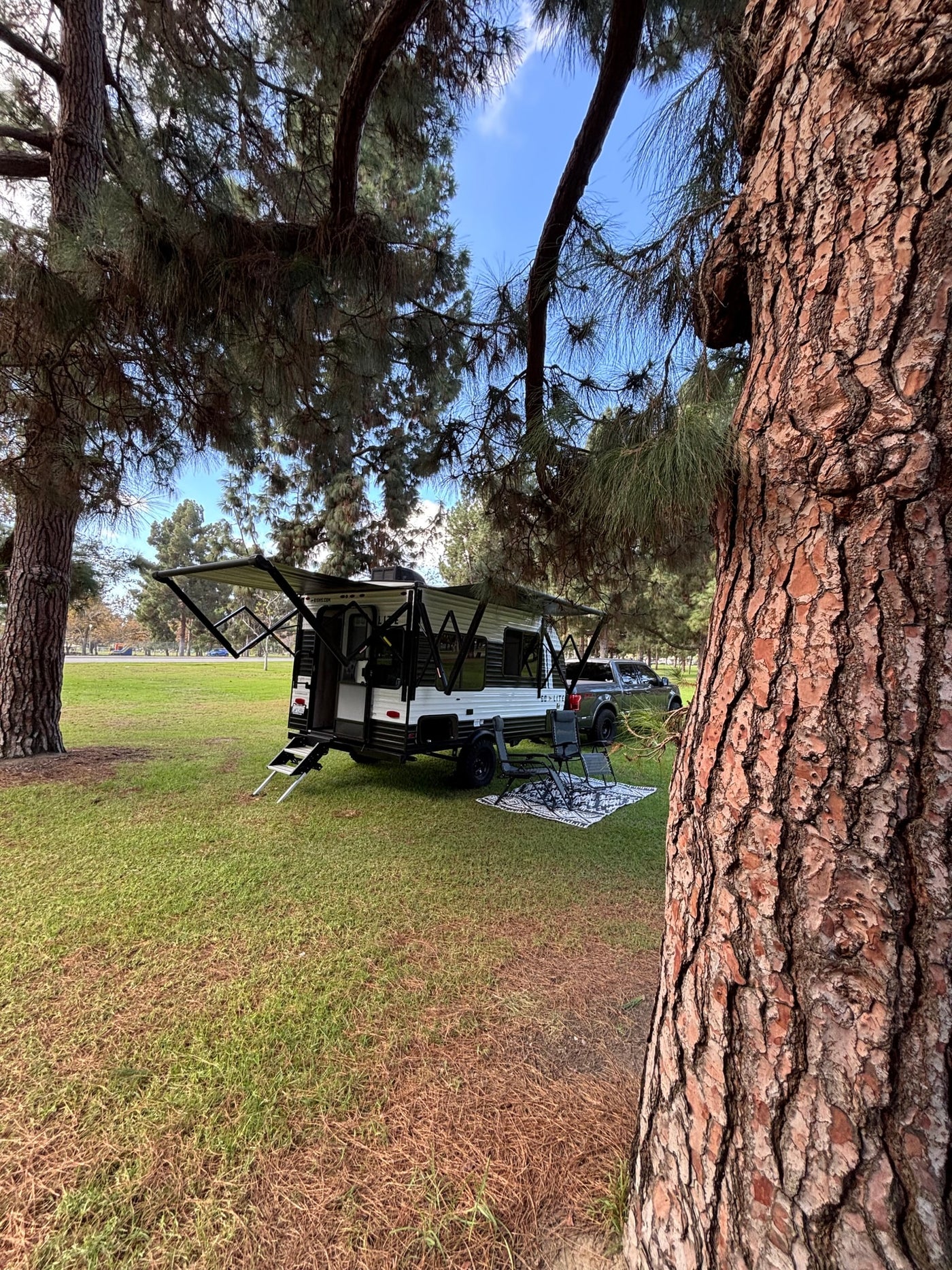 Peaceful park setup with an RV rental: a travel trailer, chairs, and truck under shade trees on green grass. Ideal for camping. — photo 3