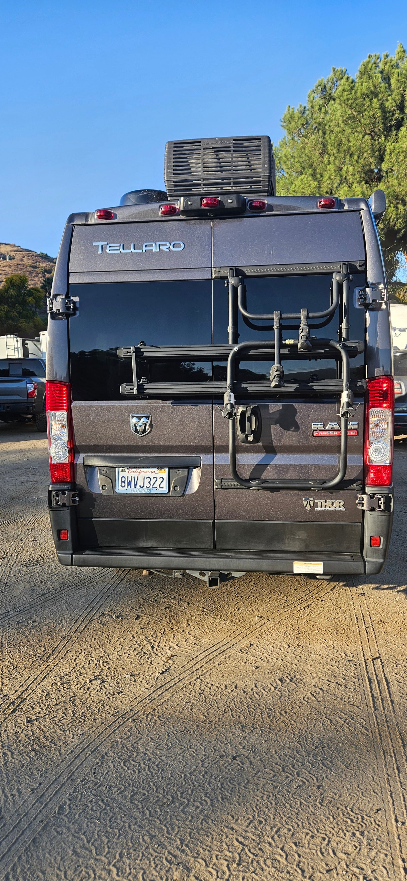 Thor Tellaro RV rental, a gray camper van with a rear bike rack, parked on dirt. Ideal for outdoor adventures.
